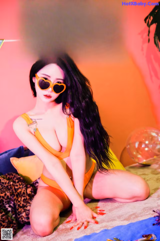 A woman in an orange bikini sitting on a bed.
