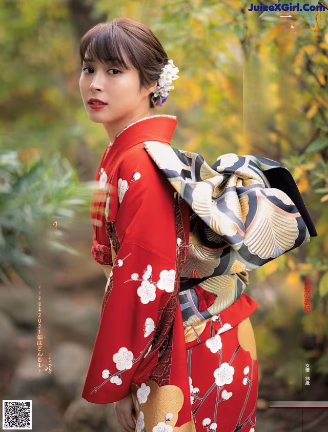 A woman in a red kimono standing in a forest.