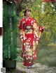 A woman in a red kimono standing in front of a tree.