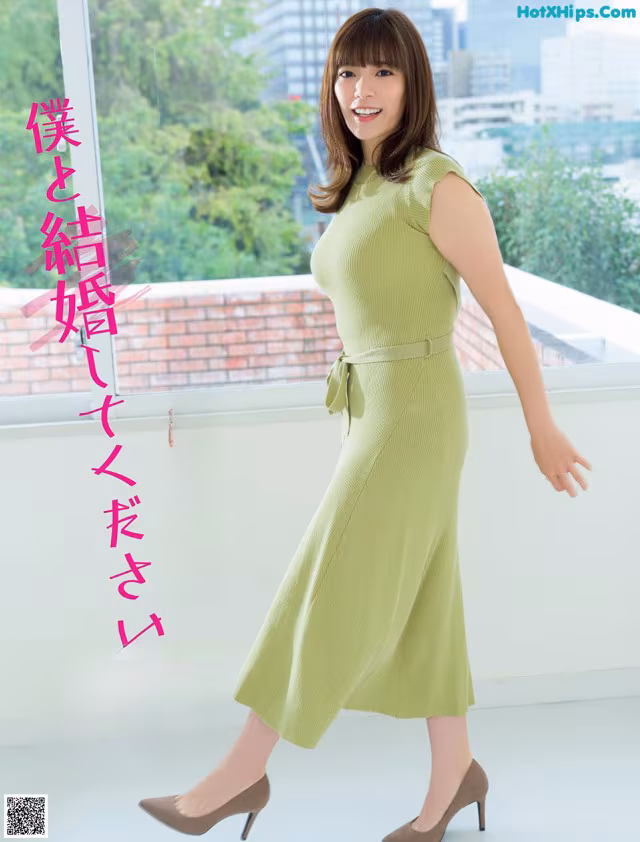 A woman in a green dress standing in front of a window.
