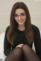 A woman wearing glasses sitting on a bed.