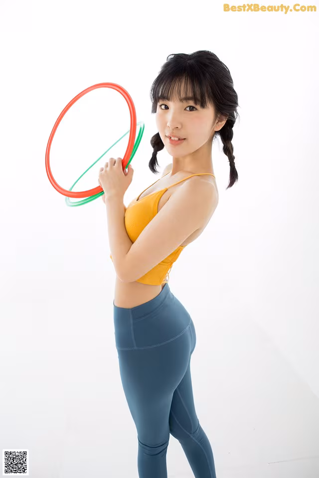 A woman in a yellow top and blue leggings holding a hula hoop.