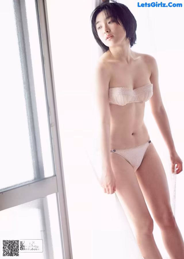 A woman in a white bra and panties standing by a window.