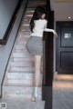 A woman in a white shirt and gray skirt is walking up some stairs.