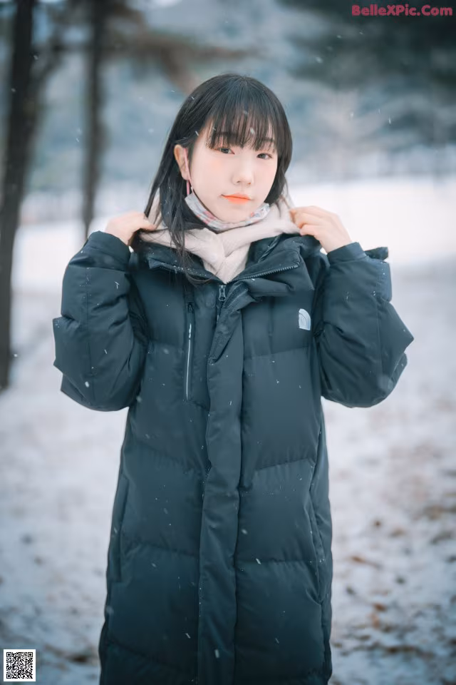 A woman wearing a black coat standing in the snow.