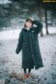A woman standing in the snow wearing a black coat.