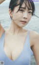 A woman in a blue swimsuit posing by the water.