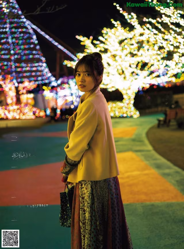 A woman standing in front of a christmas tree at night.