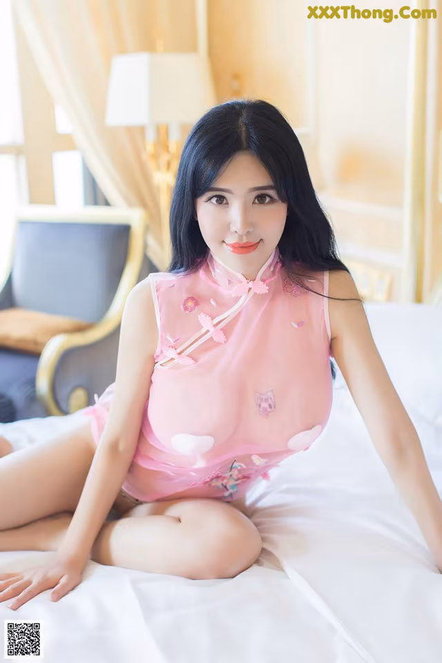 A woman in a pink dress sitting on a bed.