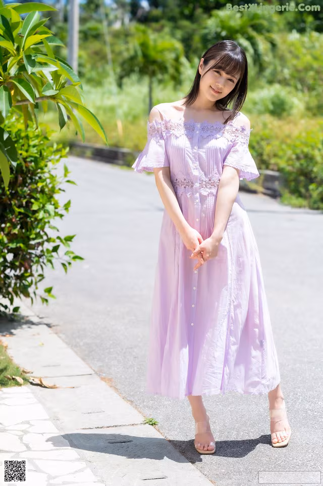 A woman in a purple dress standing on a sidewalk.