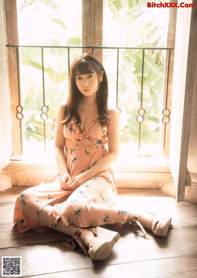 A woman sitting on the floor in front of a window.