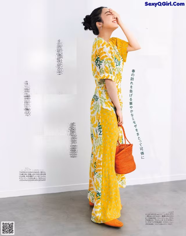 A woman in a yellow dress is standing in front of a white wall.
