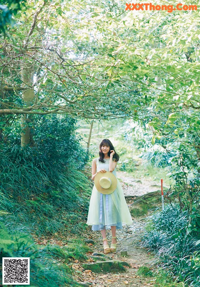 A woman in a green dress and straw hat walking down a path.