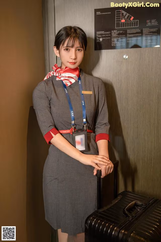 A woman in a gray dress holding a black suitcase.