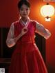 A woman in a red dress standing in front of a lamp.