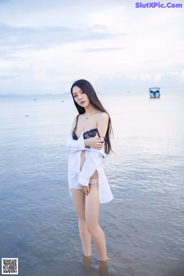 A woman standing in the water with a boat in the background.