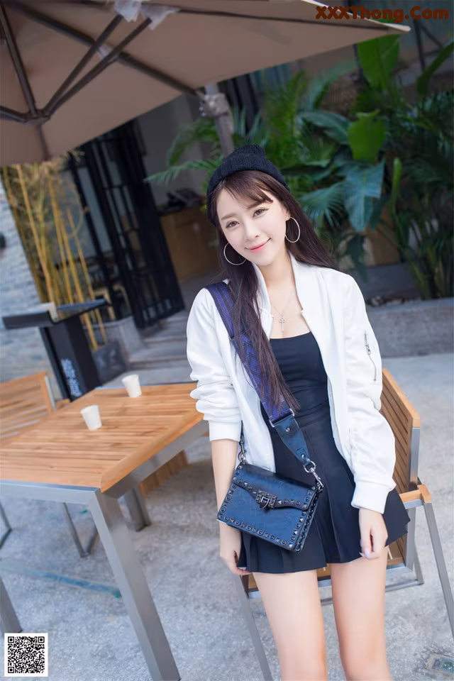 A woman in a black dress and a white jacket posing for a picture.