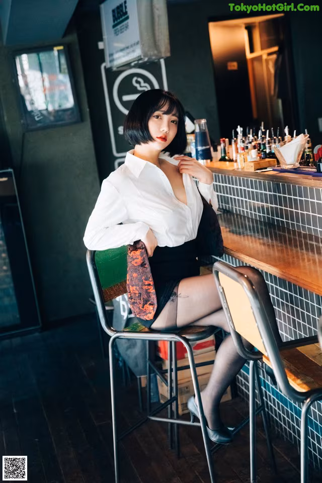 A woman sitting at a bar in a white shirt and black skirt.