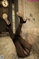 A woman in black stockings and high heels sitting on a marble counter.